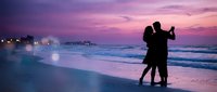 Romantic couple dancing on beach at sunset with purple pink sky and ocean waves creating intimate silhouette moment for love celebration and vacation memories.