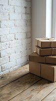 Stacked kraft paper boxes tied with twine sit on wooden floor against white brick wall with natural light from window, suitable for shipping and delivery concepts.