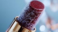 Frozen burgundy lipstick with frost crystals in golden metallic holder against blurred blue background, showcasing luxury cosmetic product in macro photography.