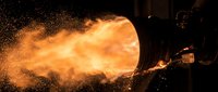 Flamethrower spraying intense orange fire and sparks against dark background, suitable for action sequences, special effects, and industrial safety materials.