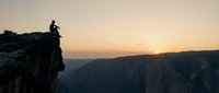 Silhouette of male hiker standing on rocky cliff edge at sunset overlooking vast canyon valley, adventure and exploration concept for travel and outdoor lifestyle.