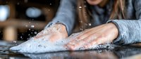Close-up of hands washing and scrubbing with soap foam and water splashes on dark surface, demonstrating proper hygiene and cleanliness practices.