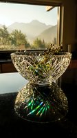 Crystal cut glass bowl with dried flowers on reflective table by mountain view window during golden hour sunset light creating rainbow prisms for luxury home decor.