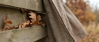 Autumn leaves nestled between weathered wooden fence boards with soft fabric draping, creating rustic fall seasonal atmosphere for home decor projects.