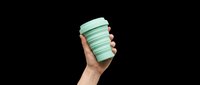Hand holding a mint green collapsible reusable coffee cup, isolated on transparent background, ready for stickers, t-shirt design, print on demand, and clipart use.