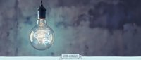 Vintage Edison light bulb glowing against dark textured wall background for interior design and creative lighting concepts.