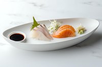 Fresh sashimi slices of salmon and white fish served on oval white ceramic plate with soy sauce, wasabi and daikon radish garnish on marble surface.