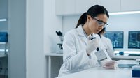 Female scientist of East Asian descent wearing white lab coat and glasses, conducting research with test tubes in modern laboratory setting for scientific research and development.