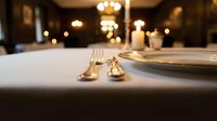 Elegant fine dining table setting with golden utensils, white linens, and warm ambient lighting in upscale restaurant interior. Perfect for hospitality, culinary, and luxury dining concepts.