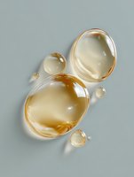 Golden transparent oil drops or bubbles floating on light gray surface with soft shadows, creating organic abstract composition with luxurious amber tones.