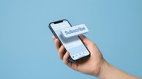 Hand holding smartphone with floating subscribe button on blue background, digital marketing and social media concept.