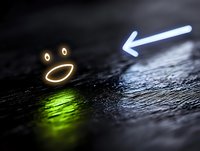 Glowing neon emoji face and arrow signs on dark textured surface with green light reflection creating modern minimalist composition for tech and social media designs.