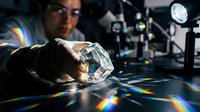 Male scientist conducting optical physics experiment with crystal prism creating rainbow light spectrum in laboratory for research and education.