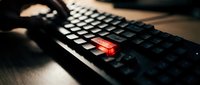 Black gaming keyboard with illuminated red key highlighted in dramatic lighting on desk surface for technology and computing concepts.