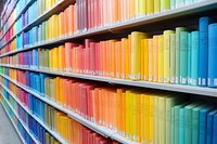 Library shelves filled with books arranged in rainbow color spectrum from blue to yellow, creating vibrant gradient pattern. Modern library interior design.
