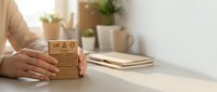 Woman holding eco-friendly cardboard coffee cup at modern workspace desk with plants and notebooks in soft natural lighting for sustainable lifestyle.