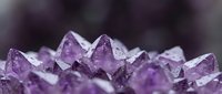 Purple amethyst crystal cluster with sharp geometric points and translucent faceted surfaces against dark blurred background for healing and meditation.