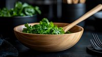 Fresh green spinach salad served in wooden bowl with utensils on dark background, healthy eating concept for restaurant menu and food blogs.