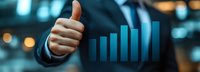 Businessman in dark suit giving thumbs up gesture next to ascending blue bar chart representing growth, success, and positive financial performance in corporate environment.