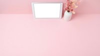 Tablet with blank screen on pink background next to dried flowers in white vase, flat lay composition for web design and digital marketing mockups.
