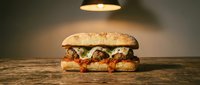 Crispy fried chicken sandwich with melted cheese, pickles and sauce on seeded bun, served on wooden surface under warm lighting for food photography and restaurant menus.