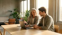 Young Caucasian couple working together on laptop at wooden table in modern office space with plants and natural lighting for business collaboration.