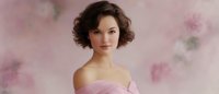 Young woman with short dark curly hair in pink strapless dress against soft floral background with dreamy romantic atmosphere, gentle makeup and natural beauty look.