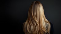 Blonde woman with long wavy hair shown from behind against dark background, highlighting natural hair movement and professional salon styling results.