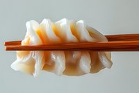 Fresh raw squid sashimi held between wooden chopsticks against light background, showcasing translucent texture and delicate folds of seafood preparation.