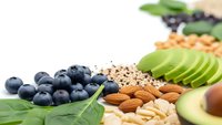 Healthy superfood ingredients with fresh blueberries, sliced avocado, almonds, walnuts and quinoa on white background for nutritious meal preparation.