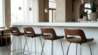 Modern bar stools with curved wooden seats and white metal legs arranged at a kitchen counter in a contemporary interior space for hospitality design.