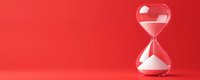 Glass hourglass with white sand on vibrant red background symbolizing time management, deadlines, and productivity concepts for business presentations.