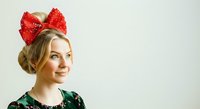 Woman wearing red sequin bow headband and green festive top, smiling against white background. Holiday portrait for seasonal marketing and celebration designs.