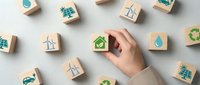 Hand holding wooden cube with green checkmark among scattered eco-friendly symbol blocks on white surface for sustainable business concepts.