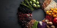 Colorful circular arrangement of fresh vegetables, fruits, nuts, grains, and berries on dark background showcasing diverse healthy food ingredients.