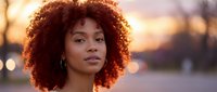 Young African American woman with curly afro hair portrait during golden hour sunset outdoors with warm lighting and bokeh background for lifestyle content.