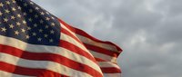 American flag waving proudly against dramatic cloudy sky background, patriotic symbol of freedom and democracy for national holidays and celebrations.