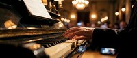Pianist hands playing piano in elegant restaurant with warm ambient lighting and blurred background creating sophisticated dining atmosphere for live music entertainment.