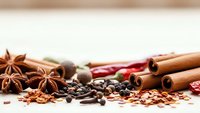 Aromatic spices including cinnamon sticks, star anise, peppercorns and chili peppers arranged on white surface for culinary cooking and seasoning.