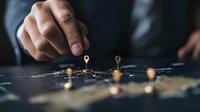 Business professional placing golden location pins on dark world map, demonstrating global expansion strategy and market targeting in corporate planning.