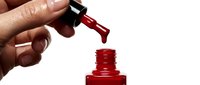 Close-up of hand applying glossy red nail polish from brush to bottle cap against white background for beauty and cosmetics use.