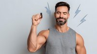 Confident mature man with beard in gray tank top holding supplement pill or medication against light background with lightning bolt graphics.