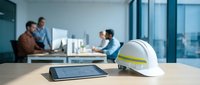 Construction team meeting in modern office with safety helmet and tablet on conference table discussing building project plans.