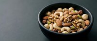 Mixed nuts and seeds in black bowl on dark background for healthy snacking and cooking ingredients.