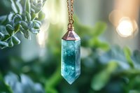 Crystal point pendant with aqua blue gemstone on bronze chain against soft bokeh green nature background, spiritual healing jewelry photography.