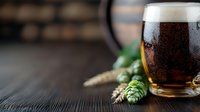 Cold glass of dark craft beer with fresh green hops and wheat ears on rustic wooden table. Selective focus on condensation droplets creates appetizing look.