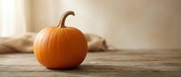 Single orange pumpkin on rustic wooden table with soft neutral background, warm autumn atmosphere for seasonal and harvest themes.