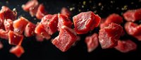 Raw beef chunks with seasoning falling on dark background, fresh meat cubes in motion capture for restaurant menu and food photography.