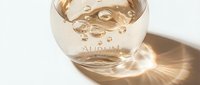 Transparent liquid in glass bottle with bubbles and golden light reflection on white background, suitable for cosmetics, skincare, perfume, and beauty product packaging design.