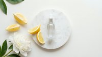 Transparent glass perfume bottle on white marble plate with fresh lemon slices and white flowers for cosmetic and beauty product marketing.
